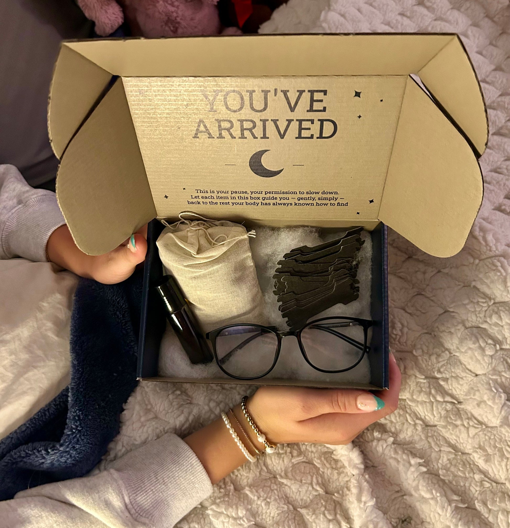 Open cardboard box with 'You've Arrived' text, containing baby items on a textured surface.
