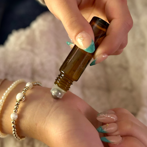Person applying essential oil to wrist with a roller bottle on a soft surface