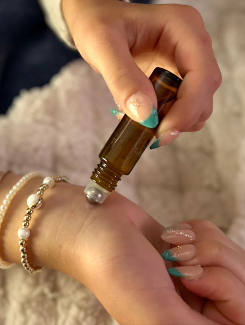 Person applying essential oil to wrist with a roller bottle on a soft surface